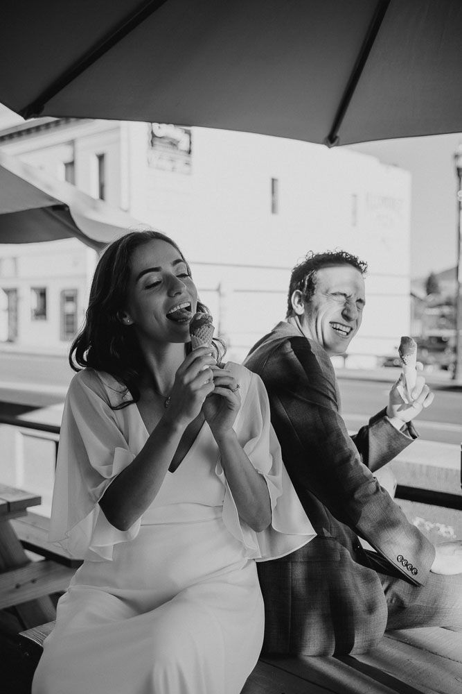 Black and white photo of couple sharing laughs while sitting under patio umbrella.