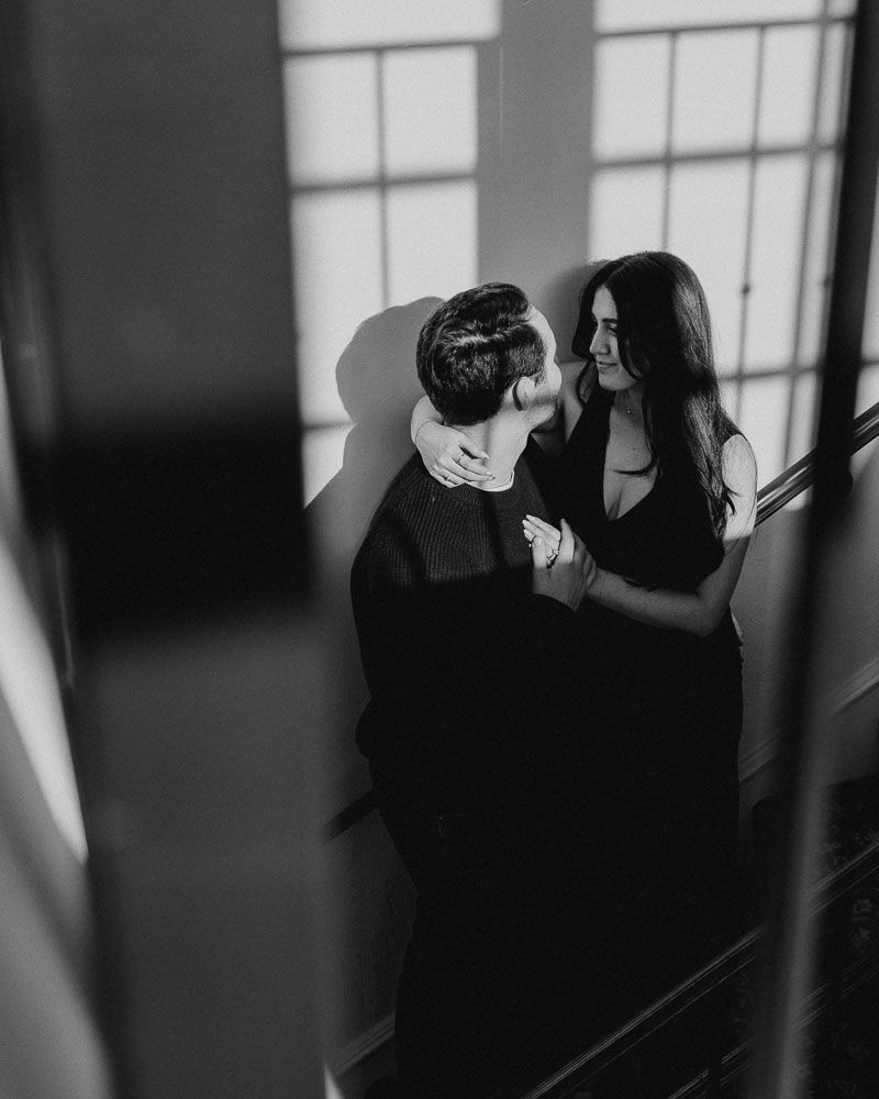 Black and white romantic portrait of a couple creating intimate shadows against a window.