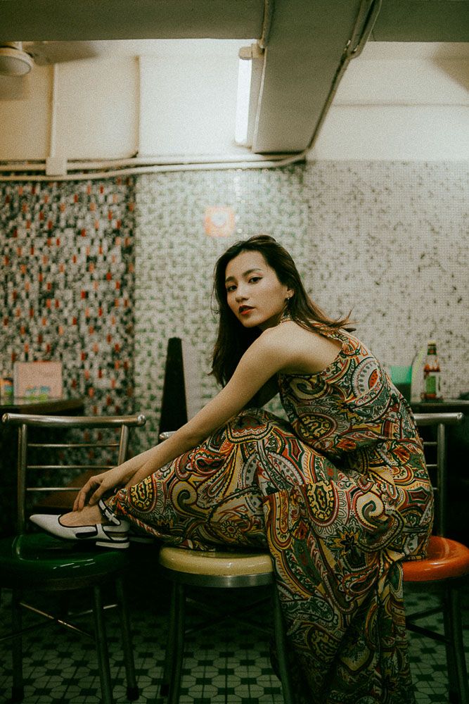 Fashion portrait in a retro diner featuring a paisley print maxi dress and dramatic lighting.