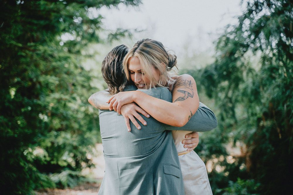 A tender embrace between two people in wedding attire surrounded by lush greenery.