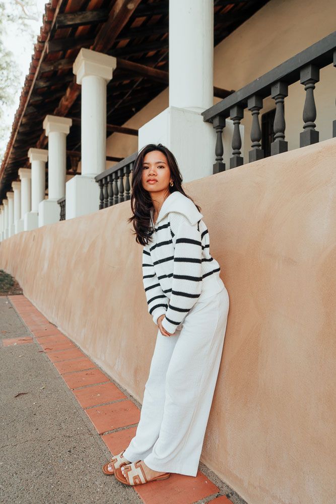Fashion portrait against colonial architecture featuring striped sweater and flowing pants.