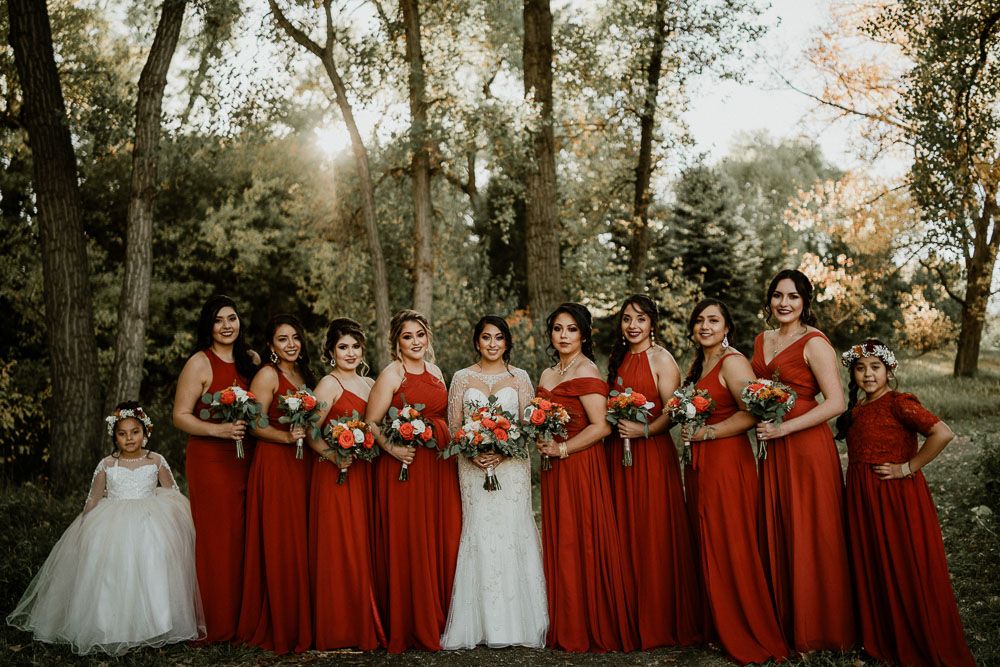 Wedding party wearing red bridesmaid dresses poses outdoors with bride in white gown.