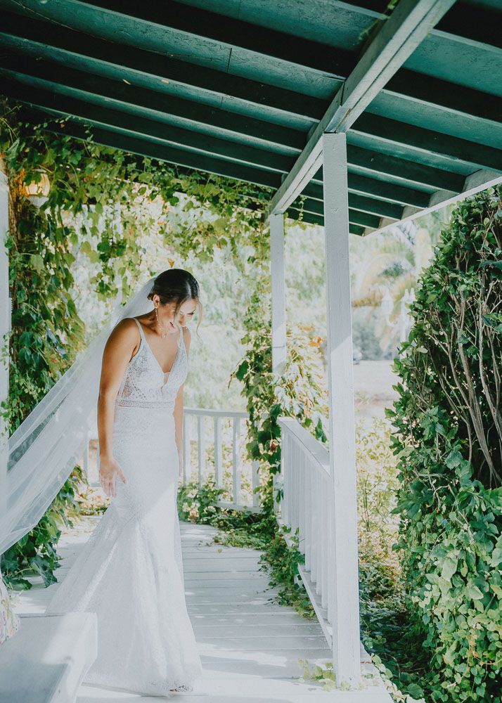 An elegant white wedding dress flows beautifully as someone walks along a vine-covered garden pergola.