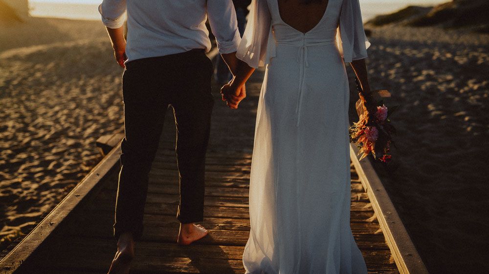 Close-up of couple walking hand in hand on beach boardwalk at sunset.