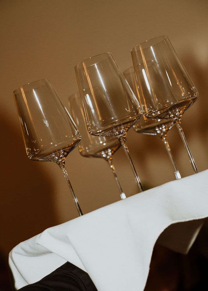 Three elegant wine glasses arranged diagonally on white tablecloth against warm brown background.