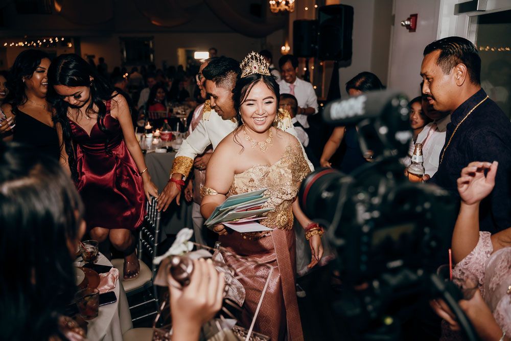 Festive celebration at a wedding reception with guests watching someone reading a card at the center of attention.