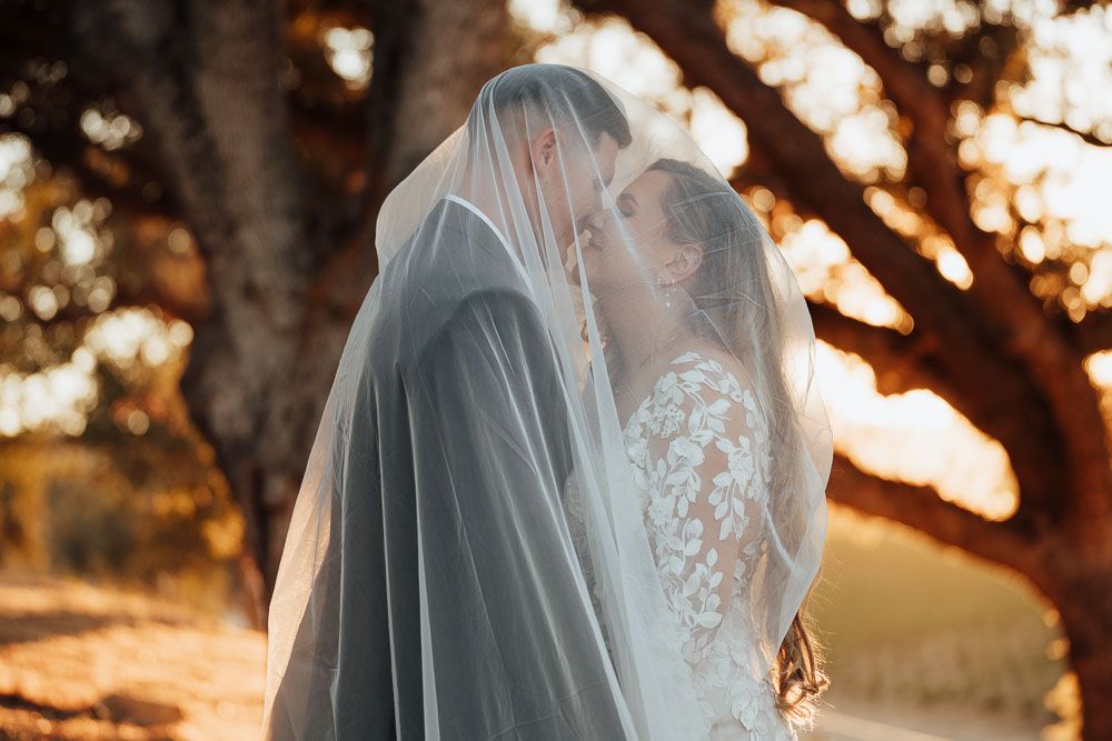 Romantic sunset portrait of a couple sharing an intimate moment under a flowing veil.