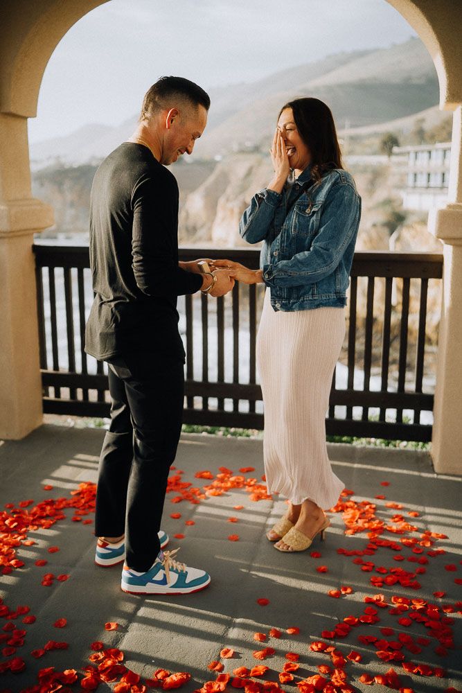 Candid proposal sequence showing couple on balcony with scattered rose petals.
