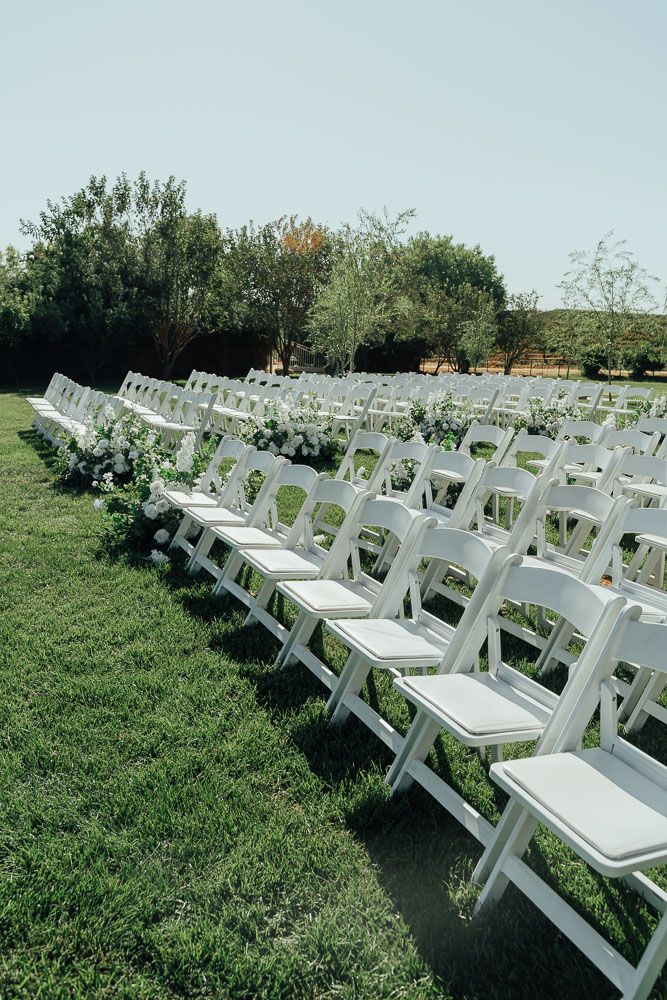 Rows of white folding chairs set up on a green lawn for an outdoor ceremony.