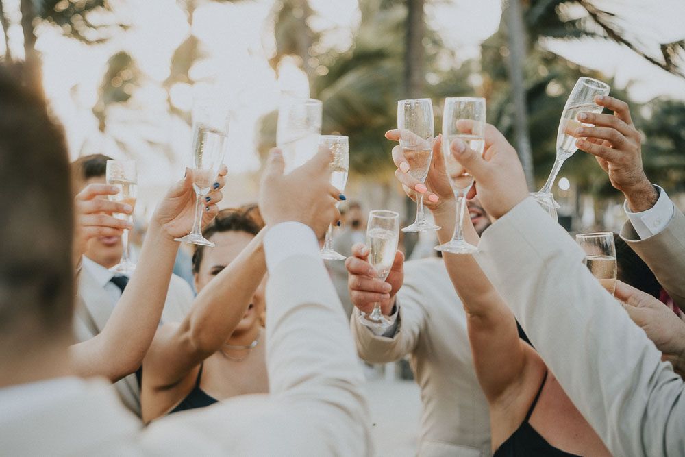 Wedding guests raise their glasses in a celebratory toast at a beachside reception.