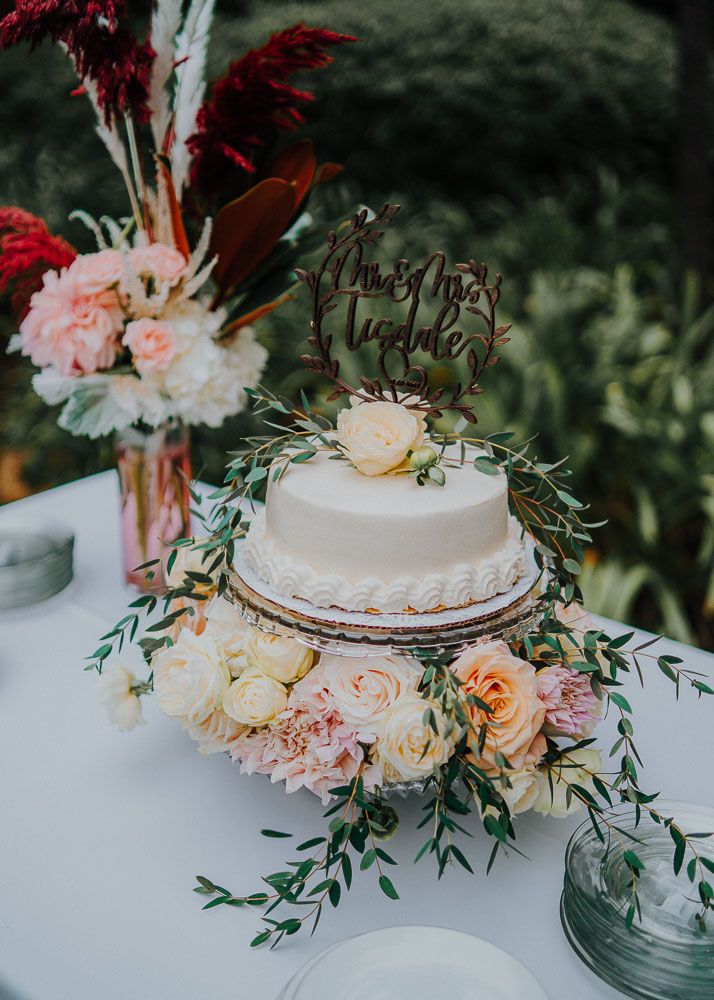 Elegant white wedding cake decorated with fresh peach and burgundy flowers and greenery.