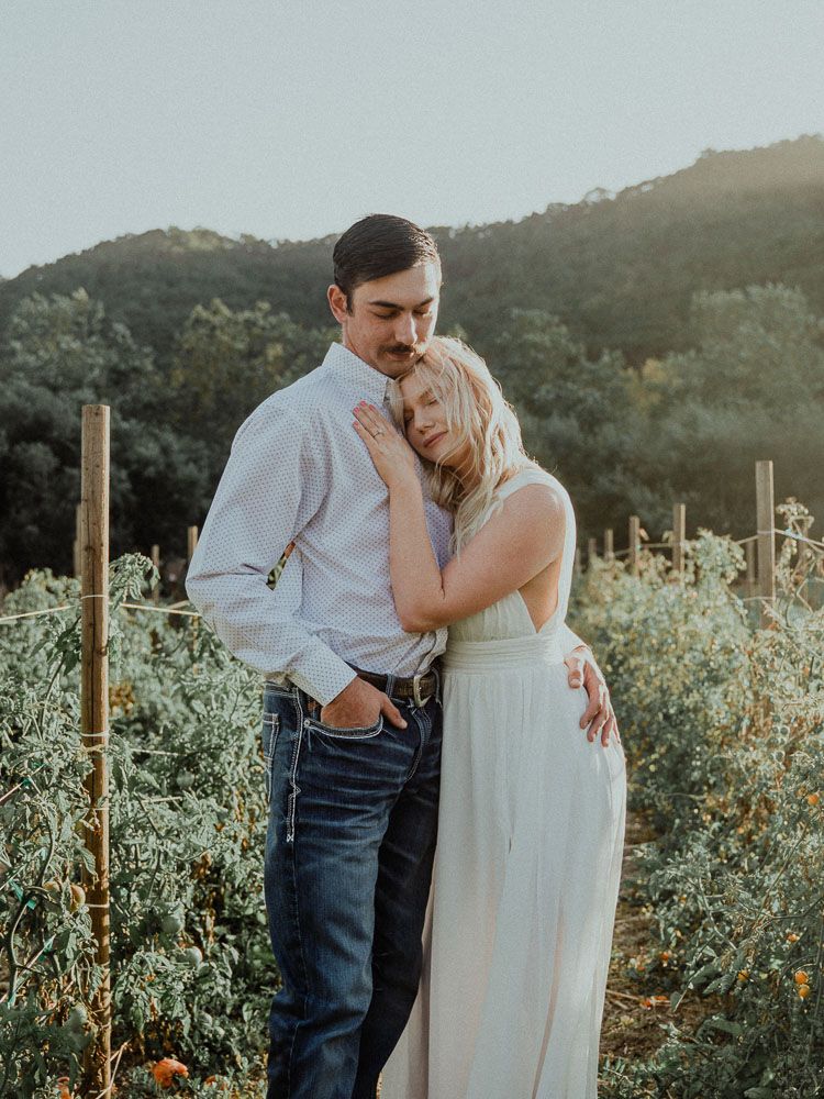 Couple embracing in white dress and casual attire against mountainous landscape.