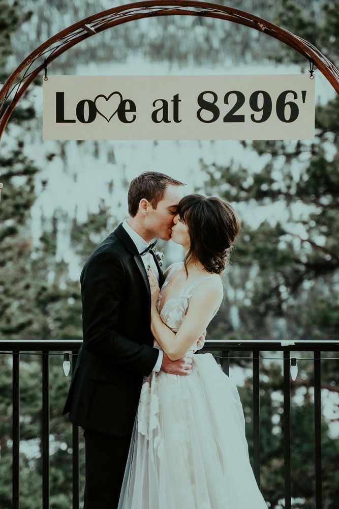 A romantic mountain wedding moment captured under an arch with 'Love at 8296' sign.