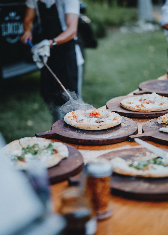 Pizza maker garnishing handmade pizzas on wooden boards at outdoor event.