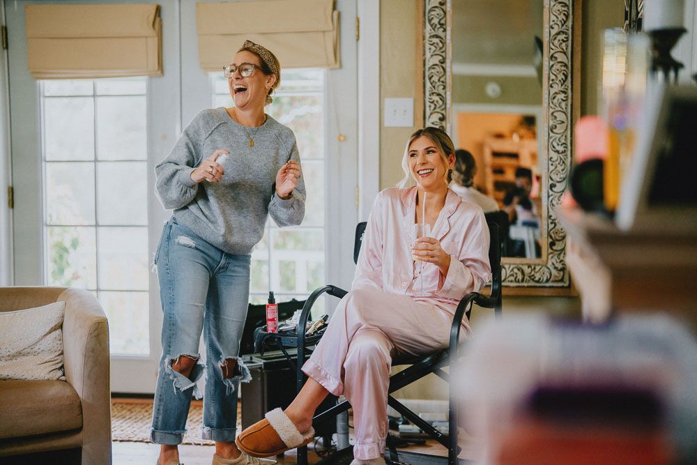 A bride and her companion laughing while getting ready