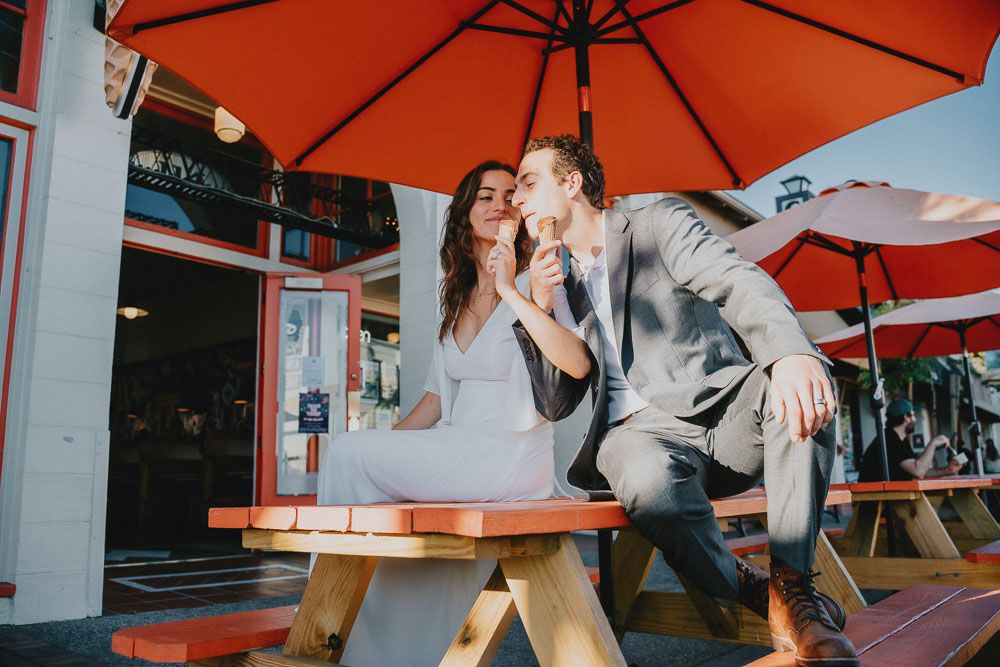 Playful couple sharing ice cream under orange umbrellas at outdoor cafe.