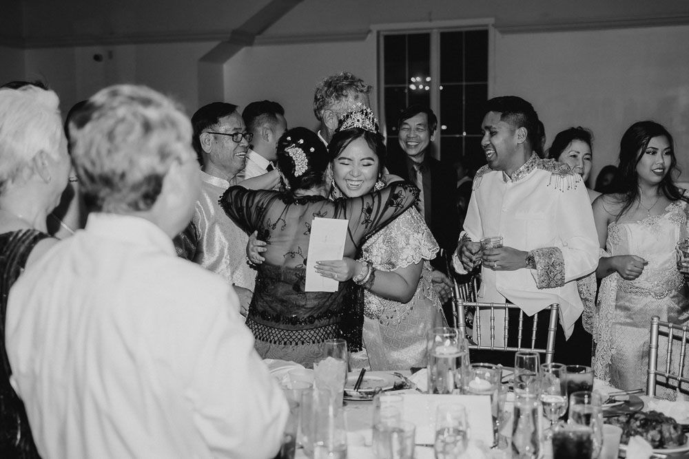 Black and white candid shot of wedding reception guests engaged in a celebratory moment.