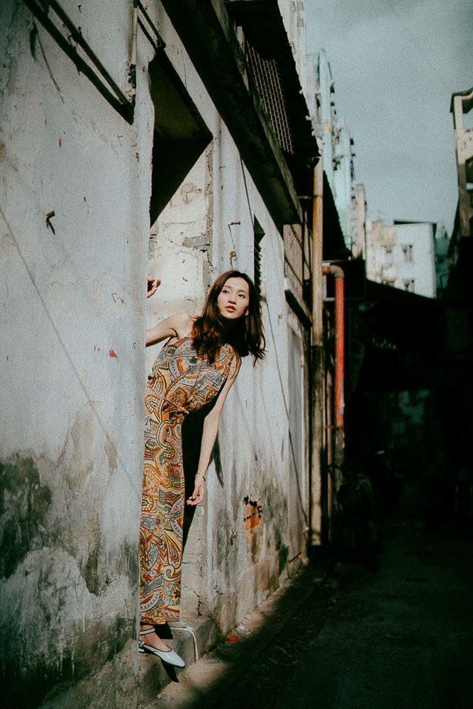 Fashion shoot along weathered white walls in a moody urban setting.