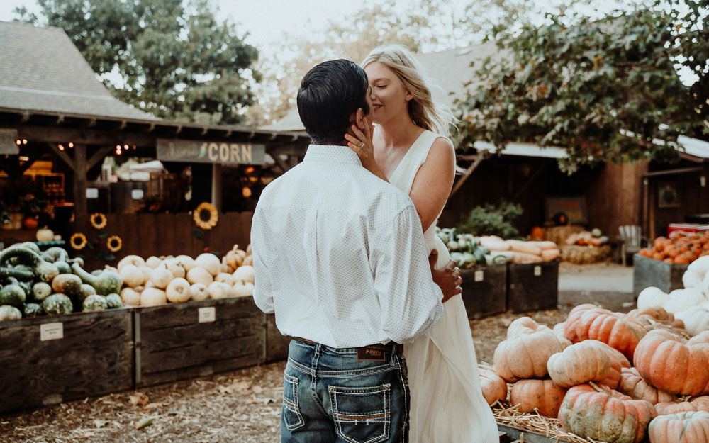 Autumn scene with couple embracing near display of pumpkins and rustic decor.