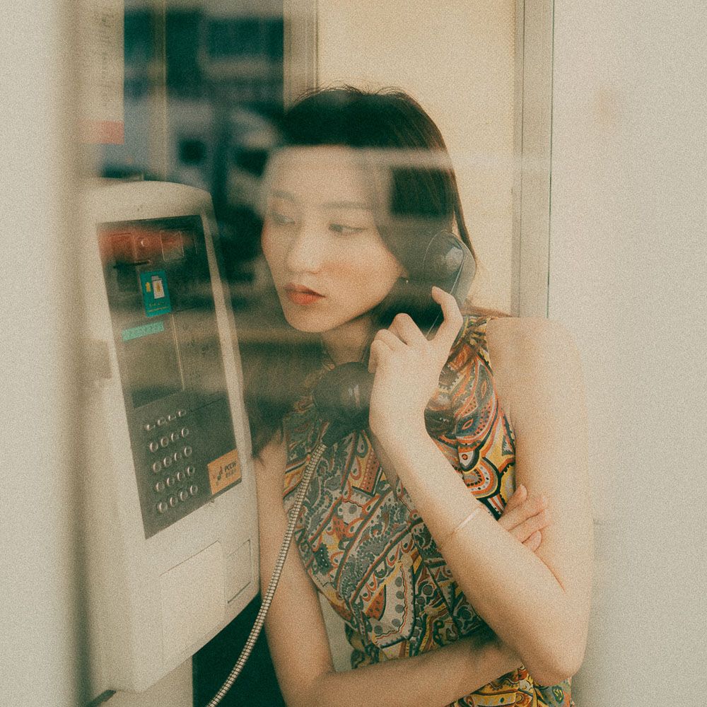 Dreamy vintage-style portrait through glass at a payphone booth.