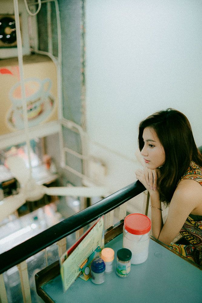 Person in a patterned dress looks contemplative while sitting at a retro diner counter with colorful containers.