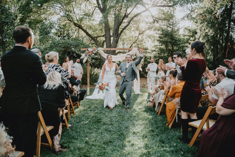Outdoor wedding ceremony with guests seated on wooden chairs as couple celebrates at the altar.