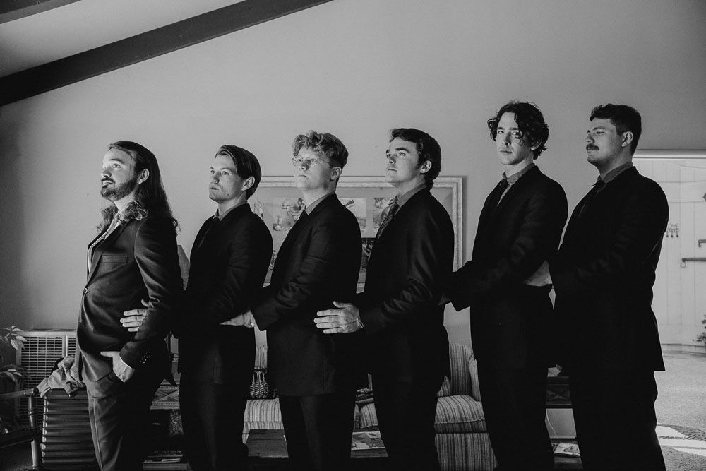 Row of men in formal attire laughing together in black and white.