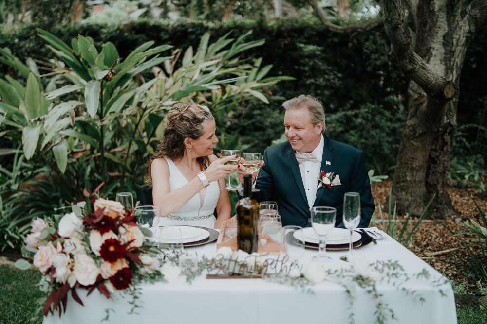 Couple shares intimate moment at outdoor sweetheart table with floral arrangements.