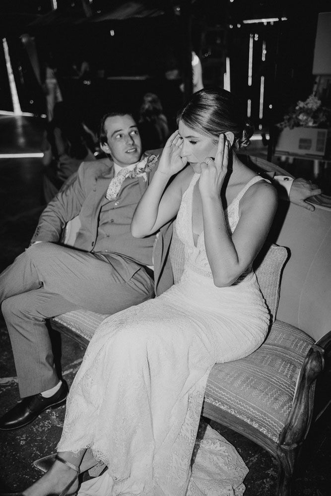 Black and white photo capturing emotional moment between couple seated on vintage couch.