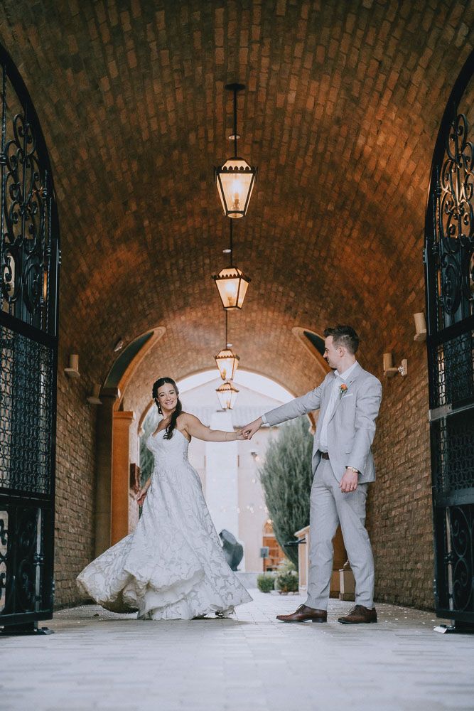 Playful wedding moment captured in brick archway with hanging lanterns.