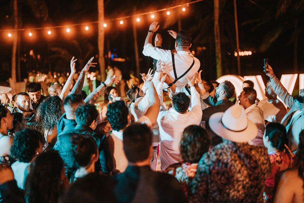 Lively crowd dancing and celebrating at an outdoor party under string lights.