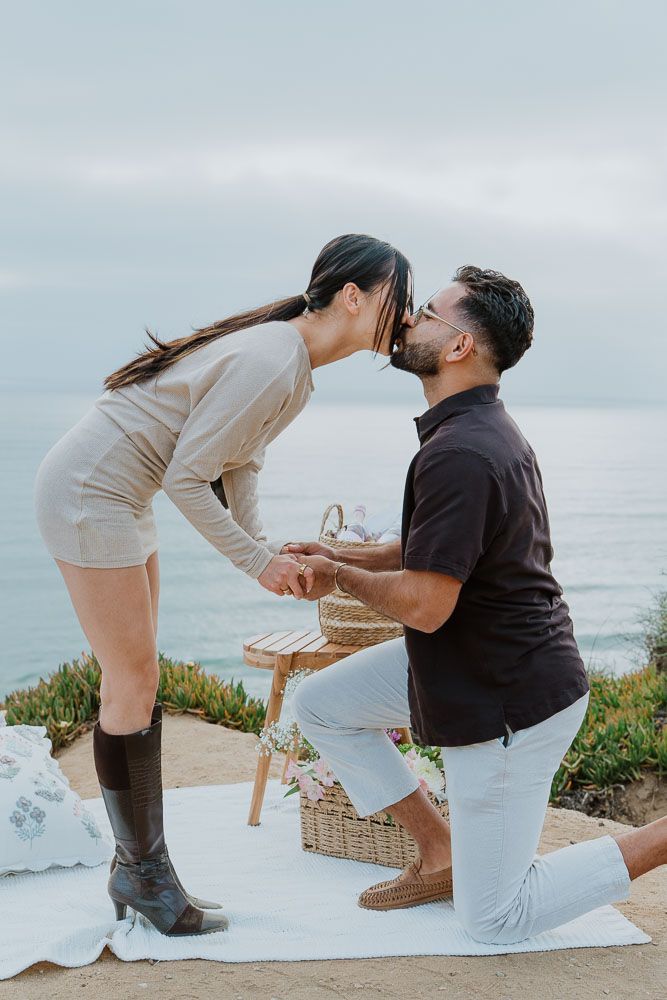 Romantic proposal scene with picnic basket by oceanside cliff.