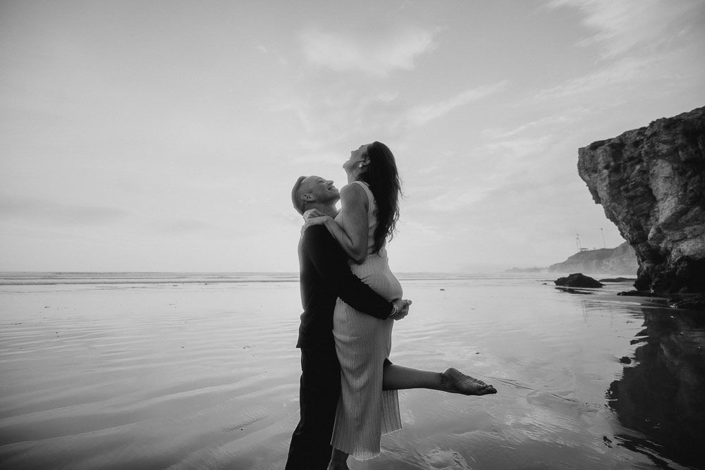 Black and white coastal photography capturing intimate moments against dramatic ocean scenery.