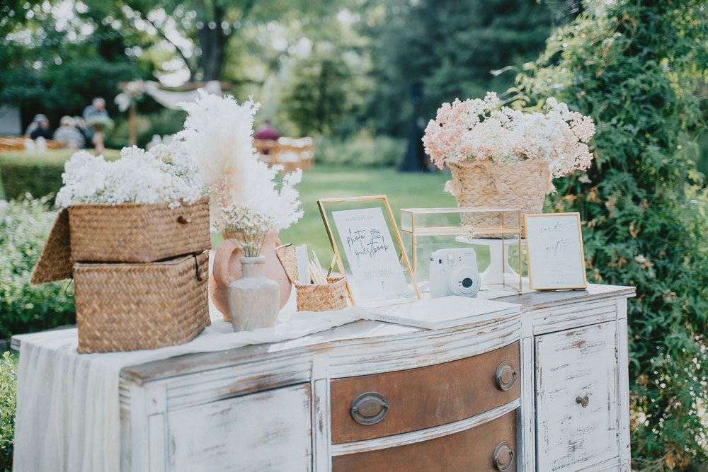 Vintage-style wedding decor with pink flowers displayed on a white distressed dresser outdoors.