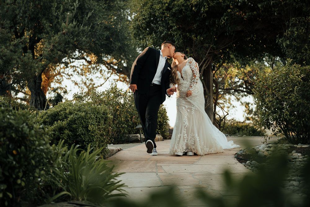 Newlyweds walking together on a garden path during sunset surrounded by greenery.