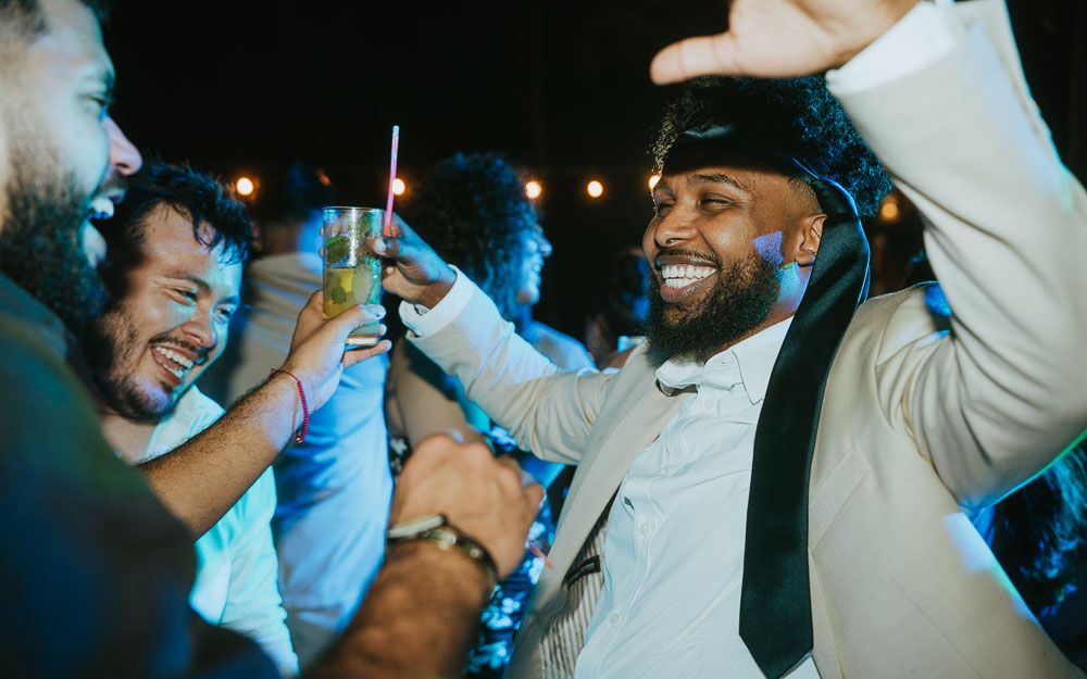 Party guests celebrating joyfully at a wedding reception with drinks raised in the air.