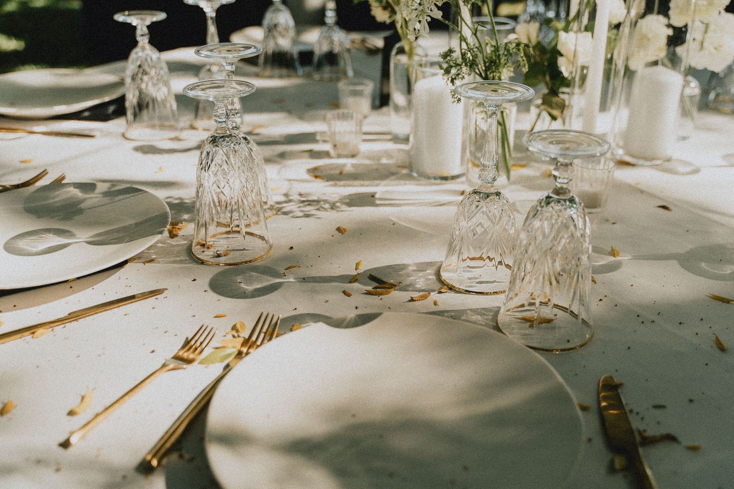 Elegant table setting with crystal glasses, gold cutlery, and white plates for a wedding reception.