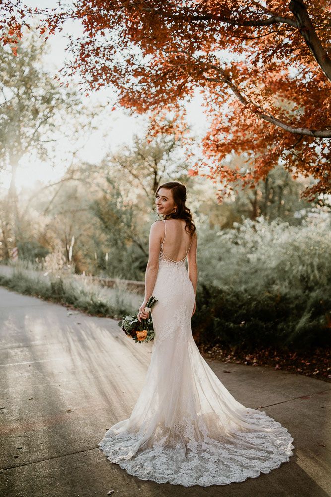 A stunning autumn wedding photo of a white lace dress train on a sunlit path surrounded by orange leaves.