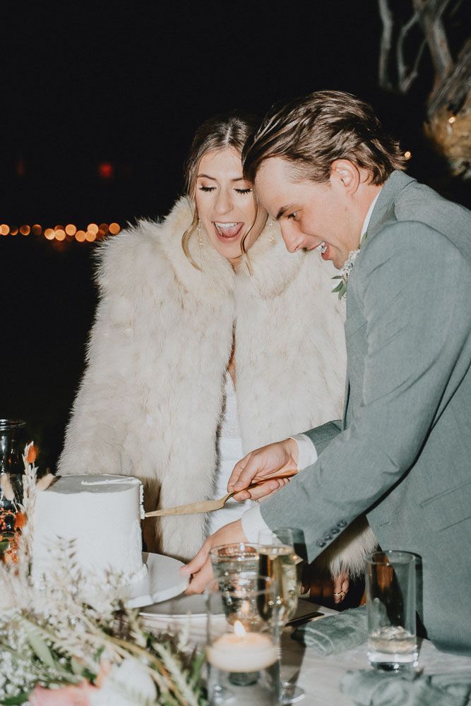 Couple sharing joyful cake cutting moment at evening reception.