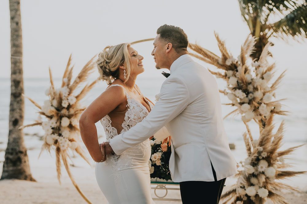 Elegant beach wedding scene with dried pampas grass decorations and palm trees.