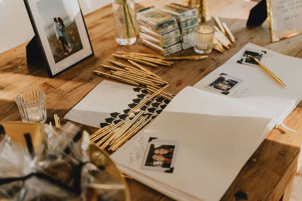 Wedding planning materials and photographs scattered on wooden table with gold details.