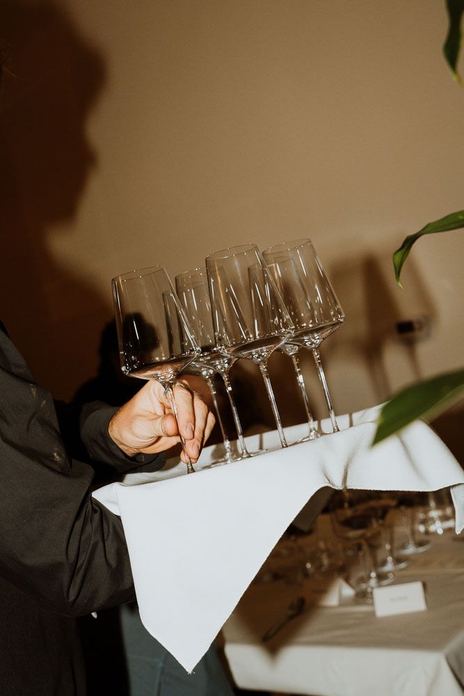 Server carrying multiple champagne glasses on white cloth at formal event.