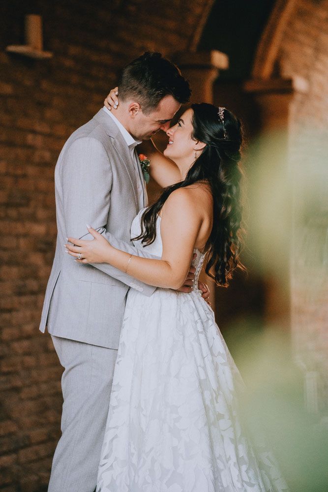 Romantic moment between newlyweds in formal attire against a brick wall with soft lighting.