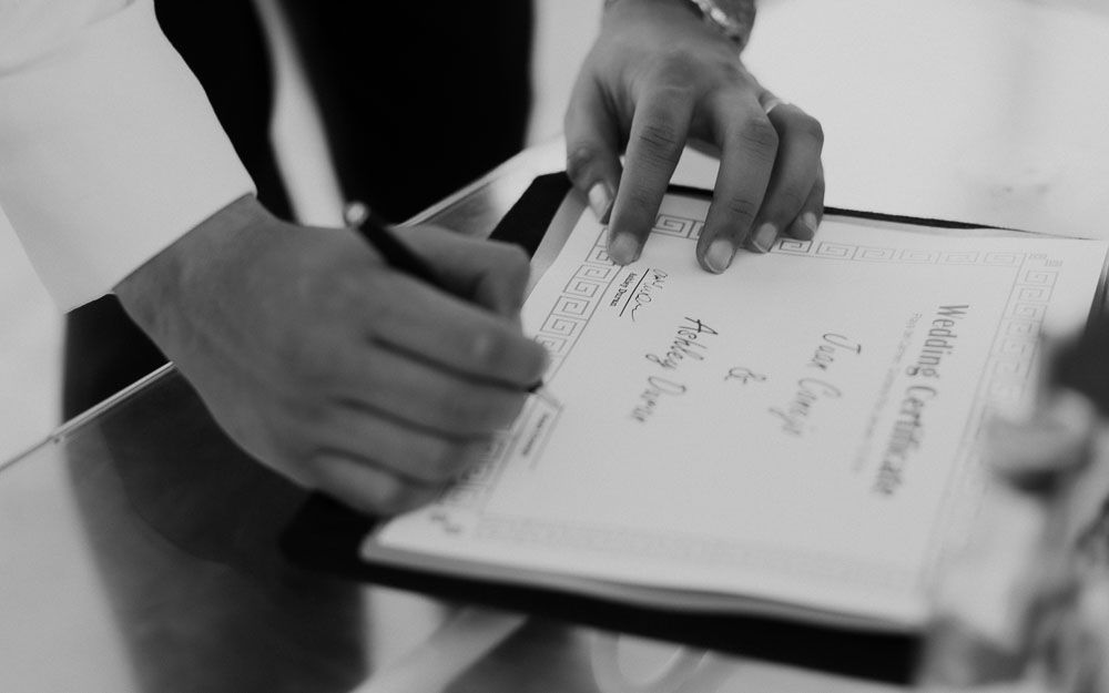 Hands writing in a notebook or document in black and white.
