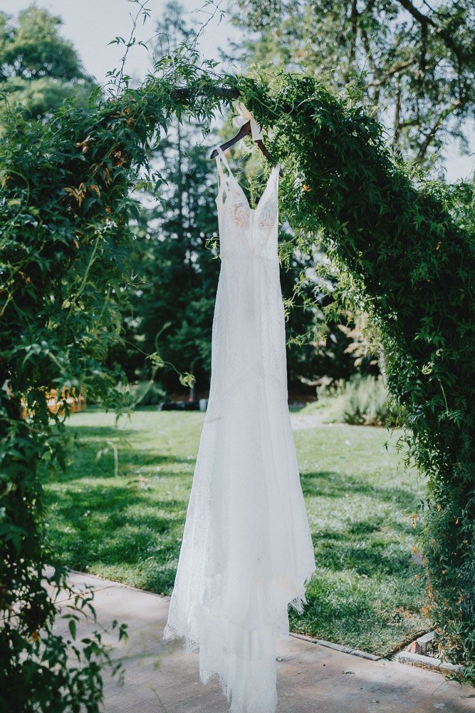Elegant white wedding dress hanging from a green garden arch against a natural backdrop.