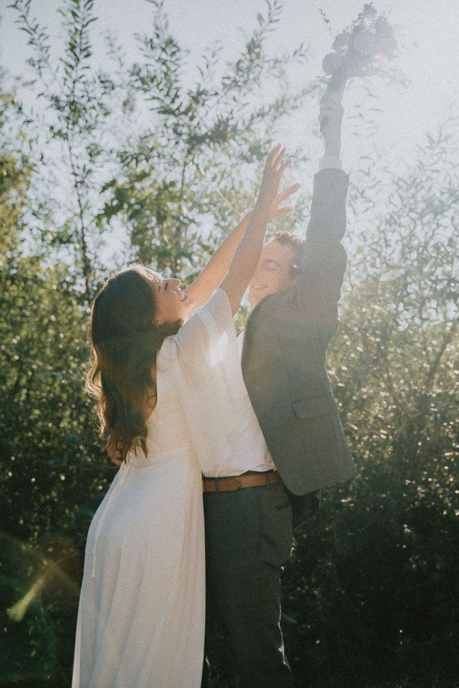 Couple in wedding attire reaching up towards the sky together in a dreamy garden setting.