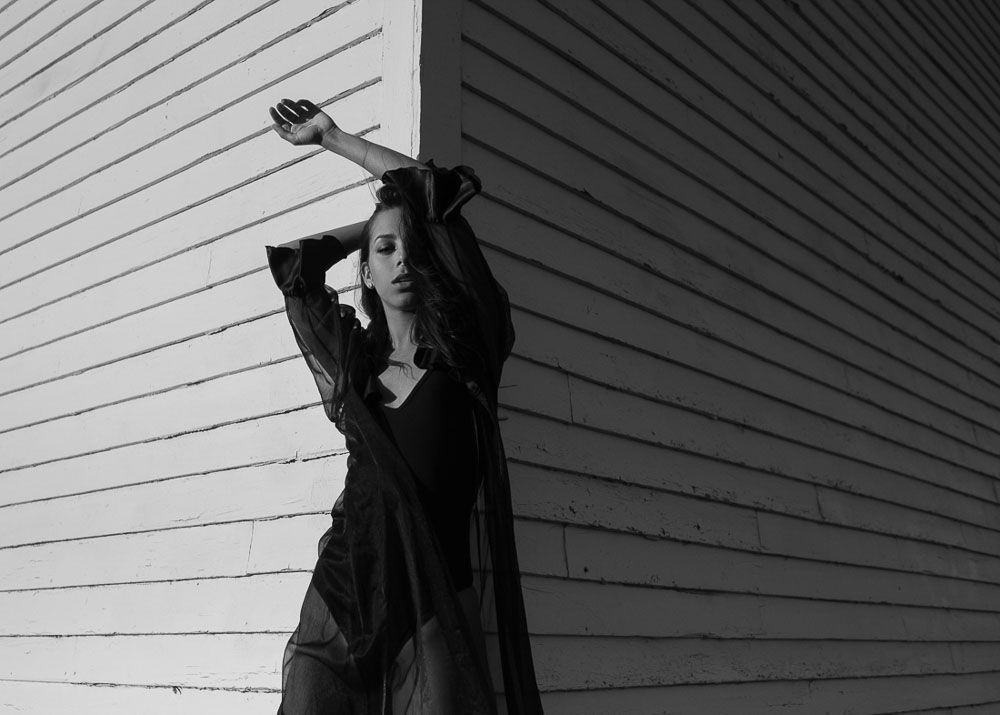 Couple embracing against white siding in dramatic black and white portrait series.