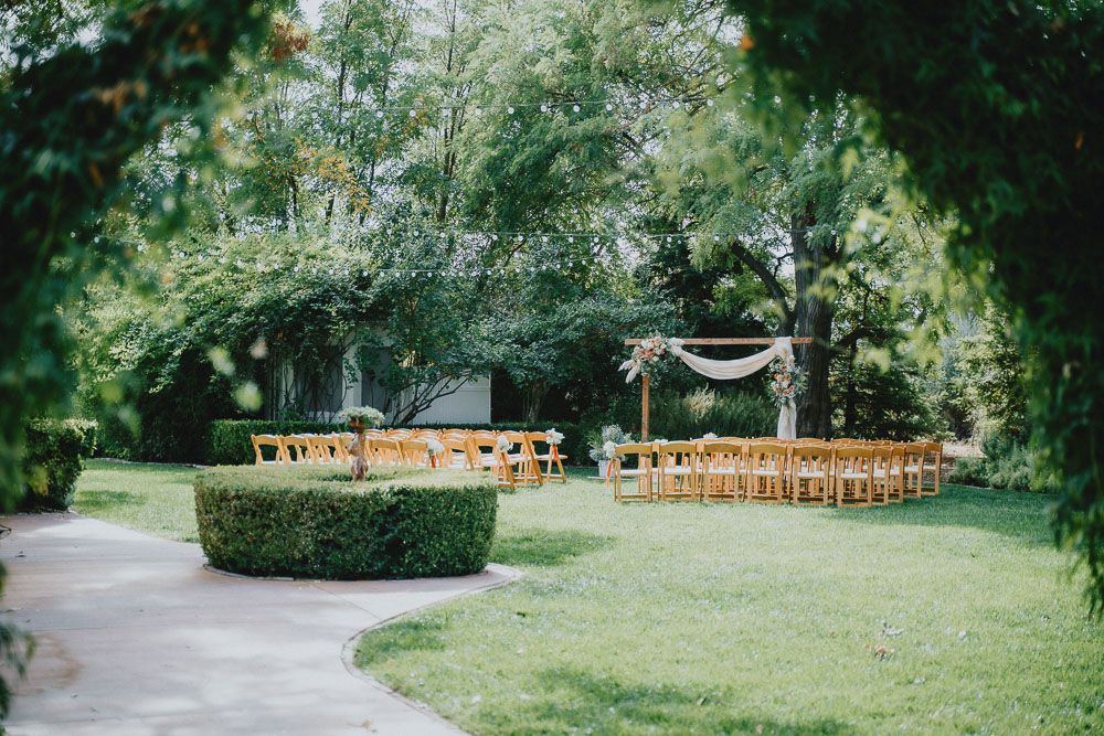 Outdoor wedding ceremony setup with wooden chairs and draped arch in a lush garden setting.