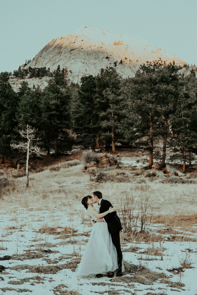 A serene winter wedding moment captured on a snow-dusted mountainside with evergreen trees.