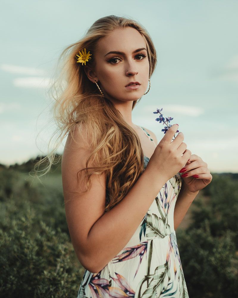 Fashion portrait in floral dress with sunflower accessory against blue sky.